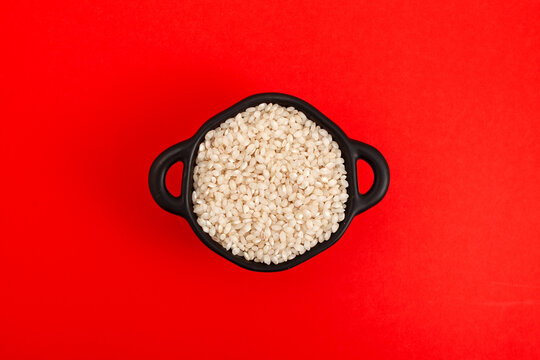 Uncooked Calasparra rice or or arroz calasparra in pan on red background, top view. Spanish processed white bomba rice ideal for paella. Natural Organic Product