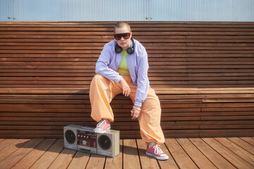 Full length fashion shot of bald young woman posing with boombox in urban city setting and wearing...