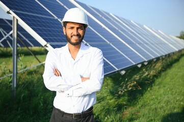 An Indian male engineer in a green vest is working on a field of solar panels. The concept of renewable energy.