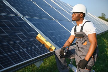 Portrait of african american electrician engineer in safety helmet and uniform installing solar panels.