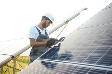 An Indian worker in uniform and with tools works on a solar panel farm