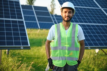 Male arab engineer standing on field with rows of solar panels.