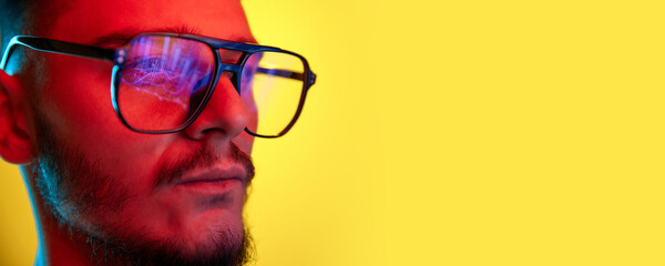 Close Up side view portrait of young handsome guy, student in glasses reflects scoring, rates, graphs isolated on yellow background in red neon light, filter.