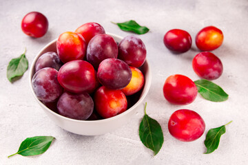 A bowl with ripe juicy plums on a gray background.