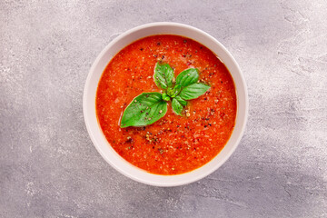 Tomato cream soup with basil and spices on gray background