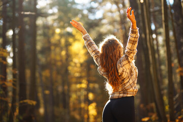 An active woman in sportswear performs yoga exercises in the autumn forest on fallen leaves,...