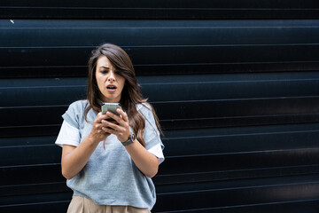 Fototapeta premium Upset and sad woman with phone in hands reading online message, Hispanic business woman received bad news notification while walking outside office building with smartphone.