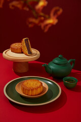Mid Autumn Festival mooncakes with elegant patterns decorated with a tea set in green color. Custom snack for Mid-Autumn Festival in China. Flower branch as foreground