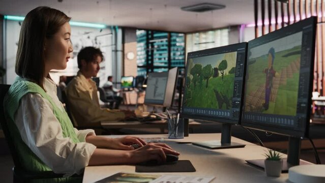 Female Asian Game Designer Using Desktop Computer, Designing Unique World And Characters In 3D modelling Software For Survival Video Game. Woman Working In Diverse Game Development Studio Office.
