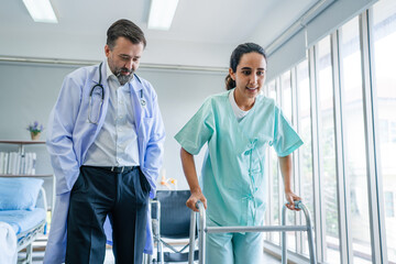 Doctor helping elderly man get out of bed and walk around the room.