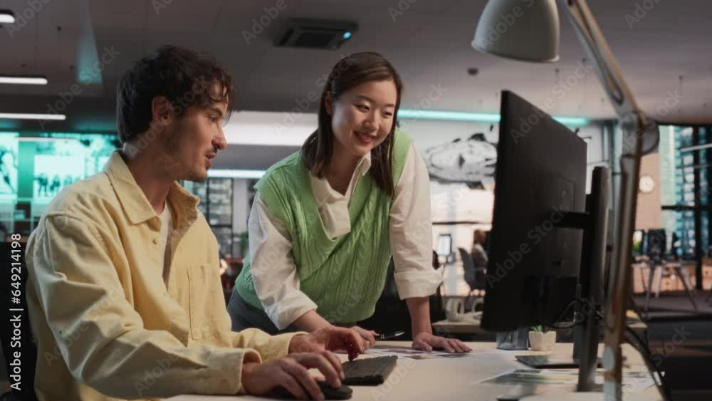 Poster Caucasian Male Game Developer Using Desktop Computer With 3D modelling Software And Talking to Asian Female Art Director in Game Design Studio Office. Diverse Colleagues Discussing New Survival Game.