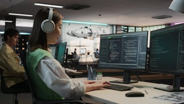 Female Asian Game Programmer Coding On Desktop Computer In Game Design Studio Diverse Office. Focused Woman Writes Lines Of Code. Gameplay Engineer of New Immersive 3D Survival Video Game Working