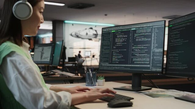 Female Asian Game Programmer Coding On Desktop Computer In Game Development Studio Diverse Office. Focused Woman Writes Lines Of Code. Gameplay Engineer of New Immersive 3D Survival Video Game Working