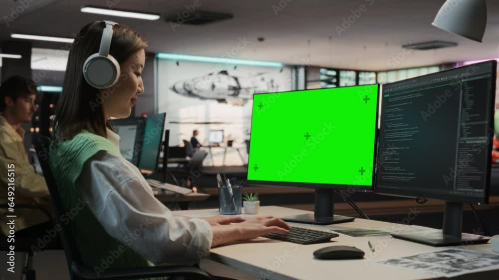 Poster Female Asian Game Programmer Coding On Desktop Computer With Green Screen Chromakey On Display In Game Design Studio Office. Stylish Woman Does Gameplay Engineering For New Immersive 3D RPG Video Game