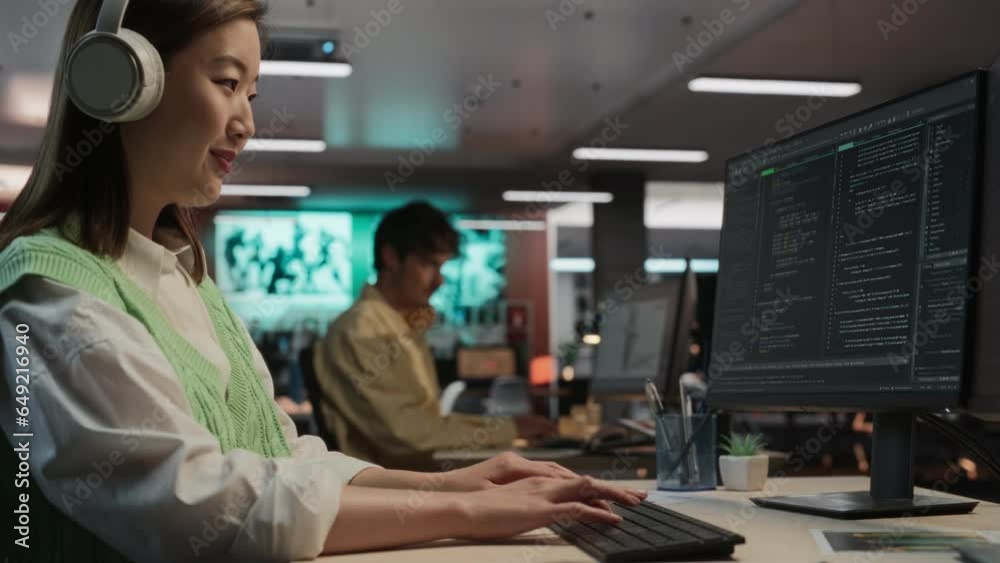 Fototapete Female Asian Game Programmer Coding On Desktop Computer In Game Design Studio Diverse Office. Woman Listening to Music, Writes Lines Of Code. Gameplay Engineer of New Immersive 3D Survival Video Game.