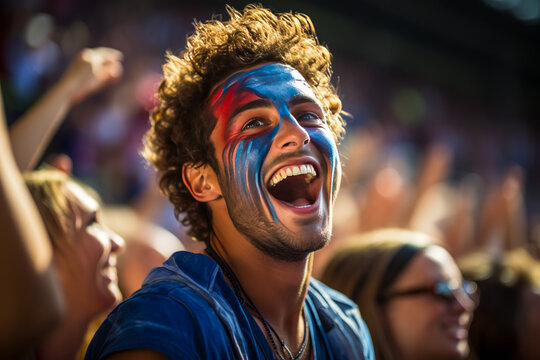 Vibrant, ecstatic young man with French flag painted on cheeks, exuding patriotism and joy amidst a blurred cheering crowd at an exciting soccer event. - Powered by Adobe