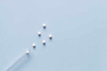 Medicine tablets closeup view with plain blue background. Homeopathic round pills and a glass...