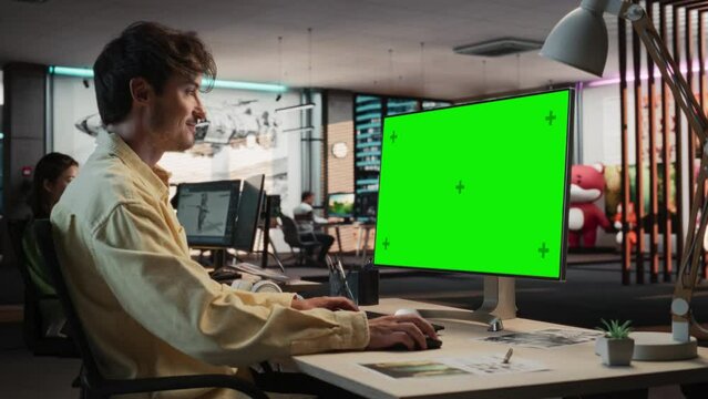 Caucasian Man Using Desktop Computer with Mock-up Green Screen Chromakey. Male Concept Artist Working in Game Design Startup Diverse Office, Creating Immersive Gameplay For New Adventure Video Game.