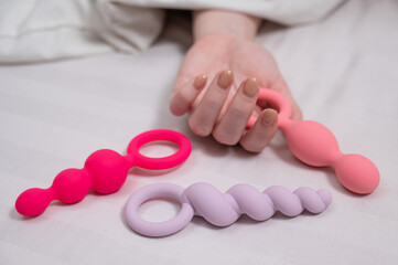 A woman chooses anal beads from a set while lying in bed. 