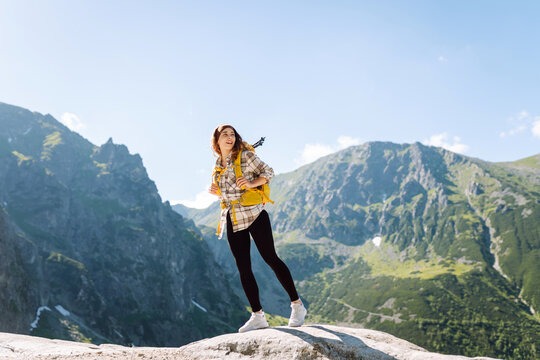 Portrait of a happy female traveler with a yellow hiking backpack standing on the top of a mountain. Concept of nature, sport, adventure.