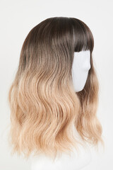 Naklejka premium Natural looking blonde fair wig on white mannequin head. Middle length hair cut on the plastic wig holder isolated on white background, side view.