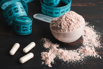 Scoop of chocolate whey protein isolate, white capsules of amino acids, creatine and measuring...