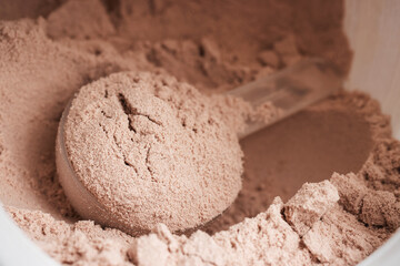Scoop of chocolate whey protein isolate in a plastic jar, close-up view