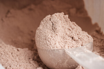 Scoop of chocolate whey protein isolate in a plastic jar, close-up view
