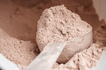Scoop of chocolate whey protein isolate in a plastic jar, close-up view