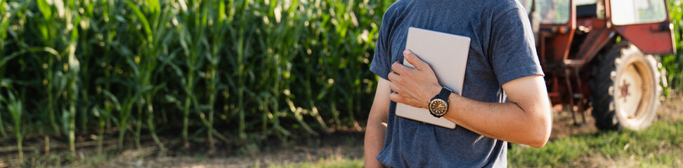 Farmer with a digital tablet is next to an agricultural tractor