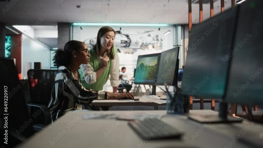 Poster Black Female Game Developer Using Desktop Computer With 3D modelling Software And Talking to Asian Female Project Manager in Game Design Studio Office. Two Diverse Colleagues Discussing New RPG Game.