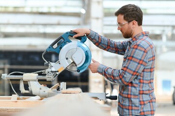 Skilled cabinet maker cutting wood board with electric circular saw at woodworking sawmill....