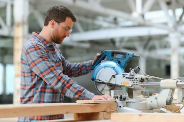 A carpenter works on woodworking the machine tool. Man collects furniture boxes. Saws furniture details with a circular saw. Process of sawing parts in parts. Against the background of the workshop.