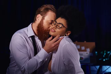 Fotobehang bearded businessman kissing smiling african american woman in eyeglasses, office romance at night © LIGHTFIELD STUDIOS