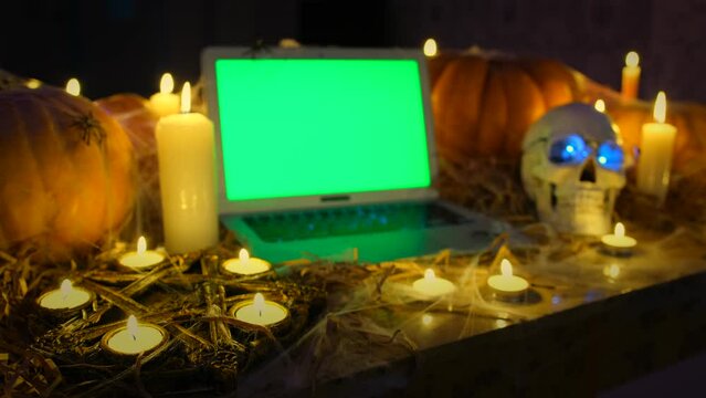 Close up, mysterious dark crypt and laptop with green screen, pentagram, flickering candles and orange pumpkins tracking shot. Celebration Happy Halloween October 31 horror invitation