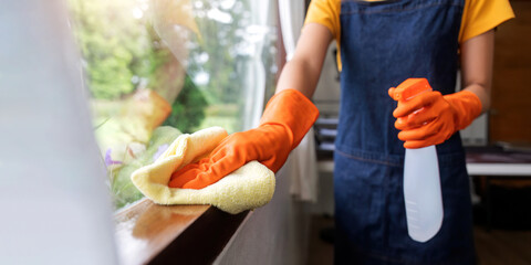 Close up hand young Asian housewife clean window glass with rag and detergent spray, cleaning house...