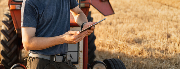 Farmer with a digital tablet is next to an agricultural tractor.