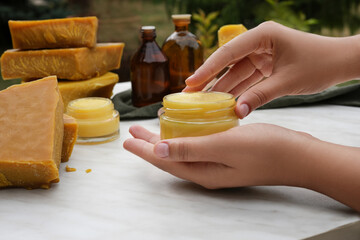 Woman hands using beeswax ointment. Medicinal cream from beeswax good for skin. Ingredients for making homemade skin cream on background. Side view. - obrazy, fototapety, plakaty