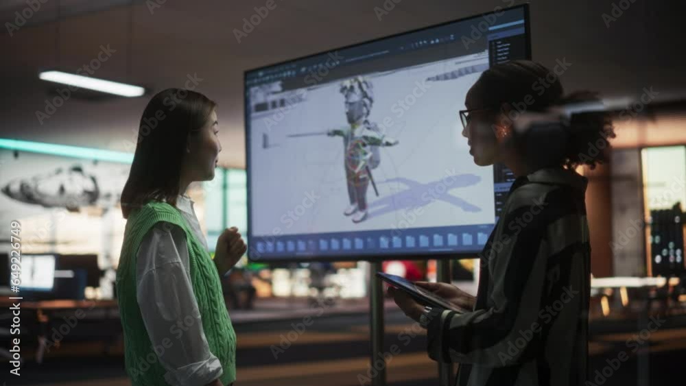 Aufkleber black female game designer talking to asian female project manager and standing next to tv set with 