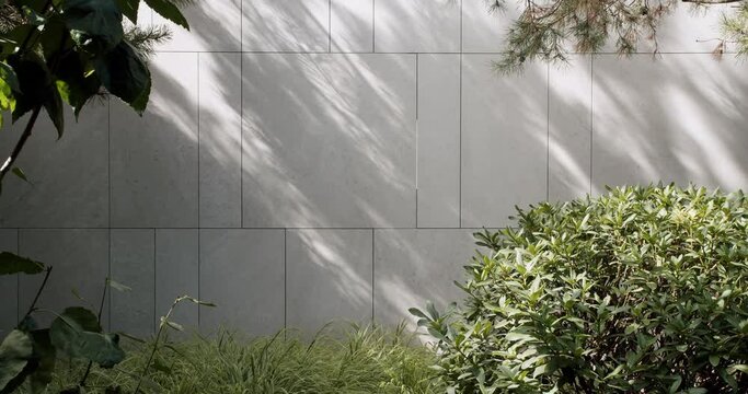 View on cottage garden yard, trees, lush bush and green grass growing on tiled wall background at sunny summer day. Sunlight and plants shadow on building facade outdoors.