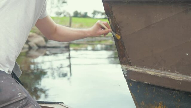 Carpenter applying polyurethane wood hardener to wooden boat bow