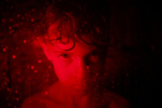 Offended boy with wet hair in red light