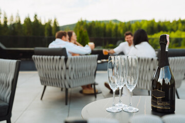 ?lose up champagne bottle and glasses with group of friends sitting on restaurant terrace on background