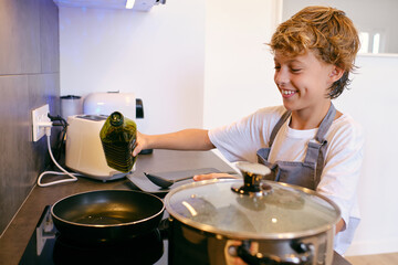 Positive boy with olive oil cooking in kitchen