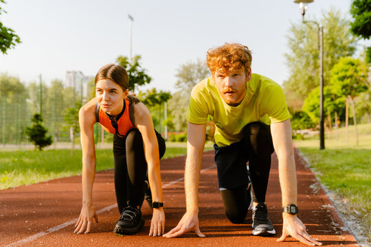 Athletic man and woman getting ready to run on sports track in park
