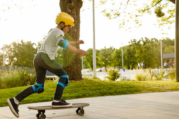 Little boy wearing safety helmet riding skateboard in park - 649240302
