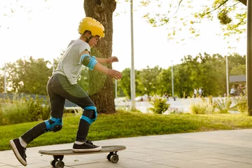 Rolgordijnen Little boy wearing safety helmet riding skateboard in park © Drobot Dean