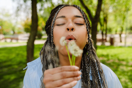 Young Woman Blowing Dandelion Flower In Park