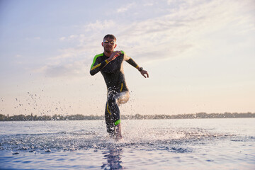 Sportive man in wetsuit and goggles training in early morning. Triathlete running in river, swimming. Concept of professional sport, triathlon preparation, competition, athleticism