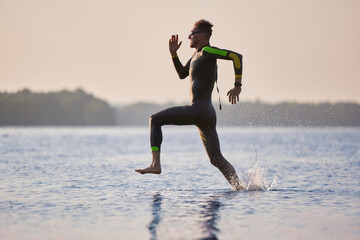 Professional triathlete, sportsman in wetsuit running into water for swimming training. Speed and...